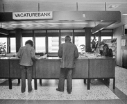 880674 Afbeelding van enkele personen die zoeken in de bakken met vacatures in de Vacaturebank in het Arbeidsbureau ...